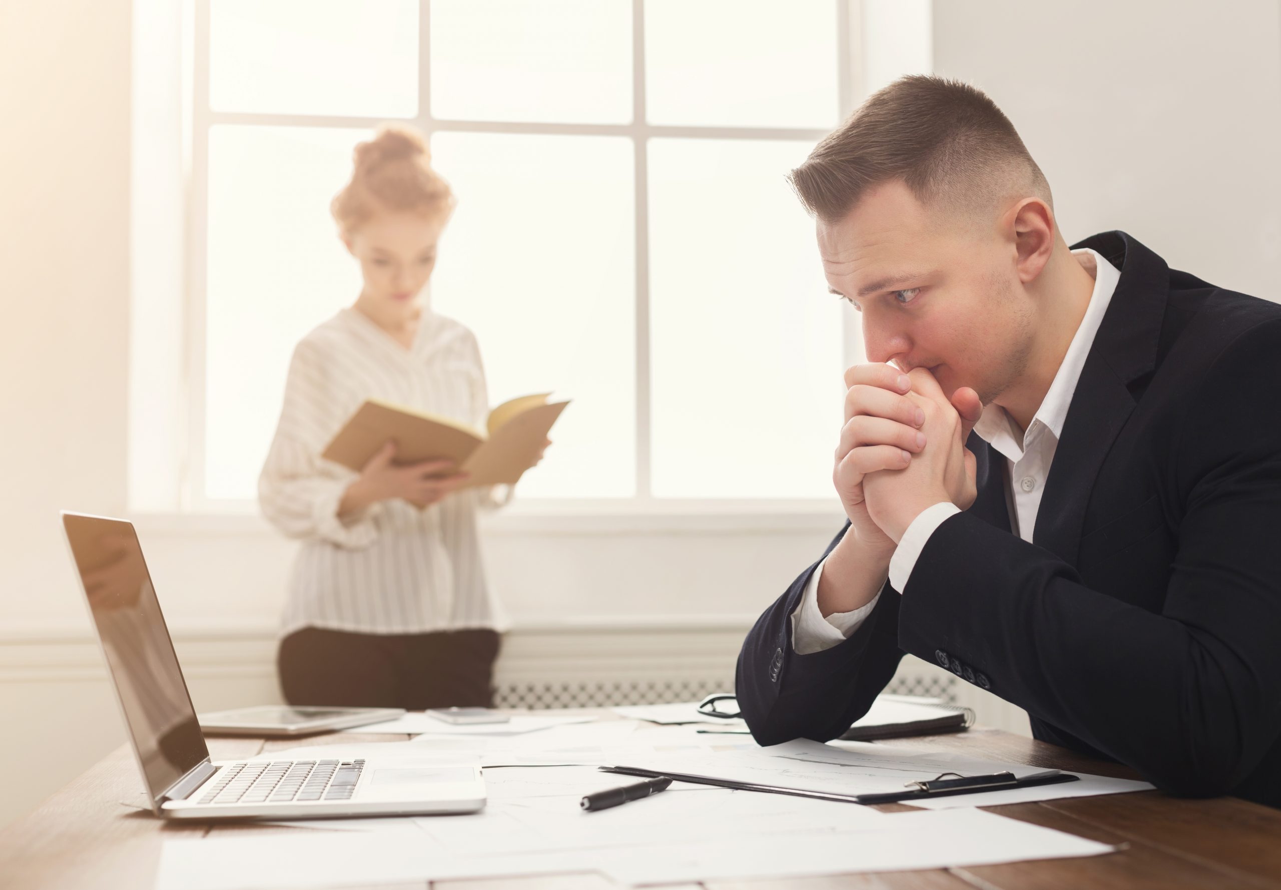 Business partners working at office. Serious and tired managers developing marketing strategy at modern workplace with laptop and papers, copy space, selective focus